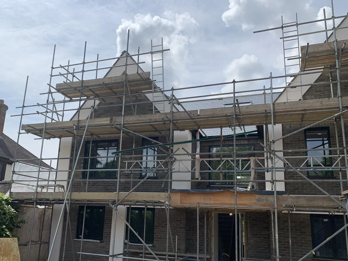New detached house in Brentwood under scaffolding, with rendered piers between brick sections and gables