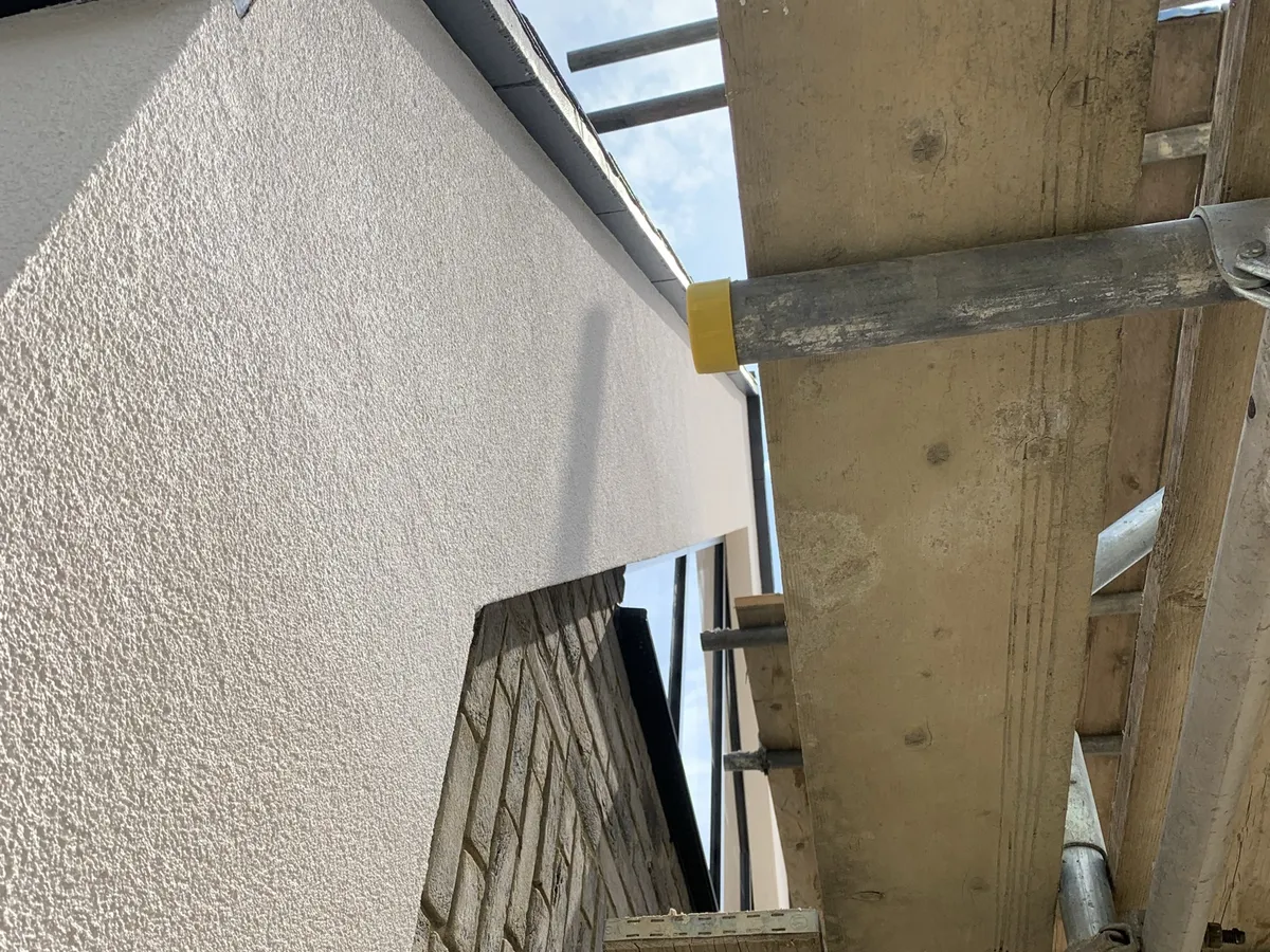 Close view of a fine textured off-white render finish meeting brickwork on a new build