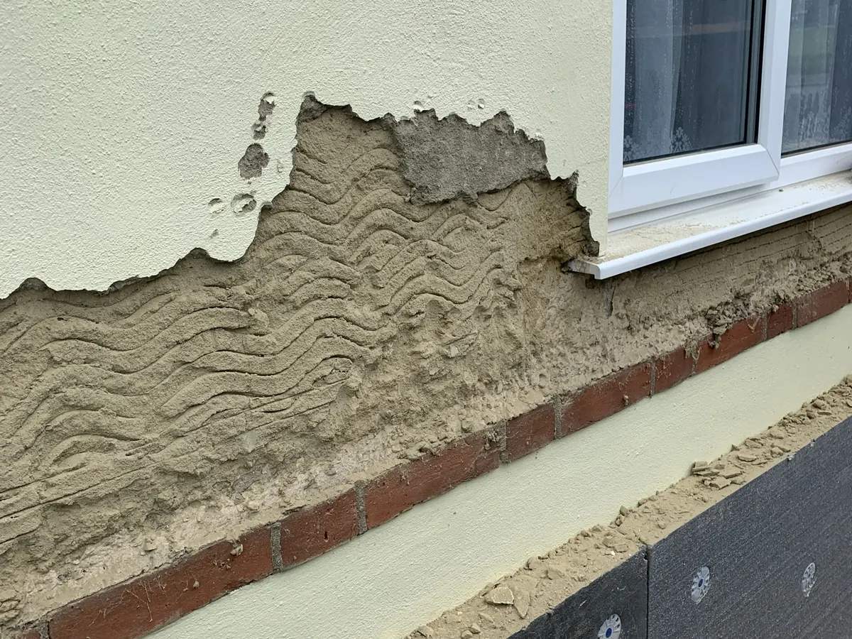 Old render failing and coming away from a bungalow wall in Hertfordshire, with insulation boards fixed below