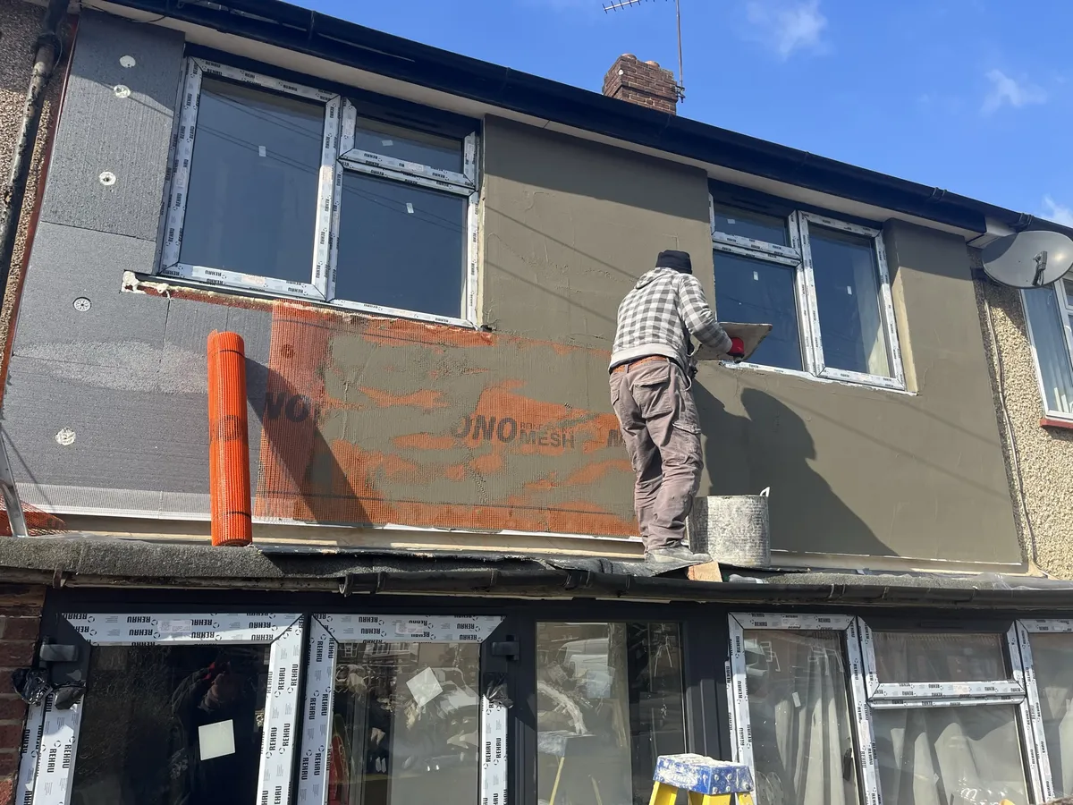 Plasterer bedding orange reinforcing mesh into the base coat over insulation boards on a Hornchurch terrace