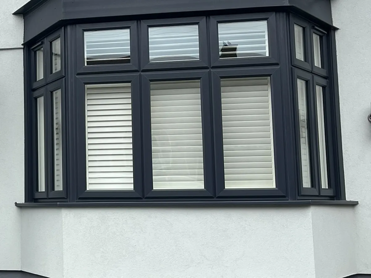 Close view of a ground floor bay window finished in light grey silicone render with a dark grey plinth