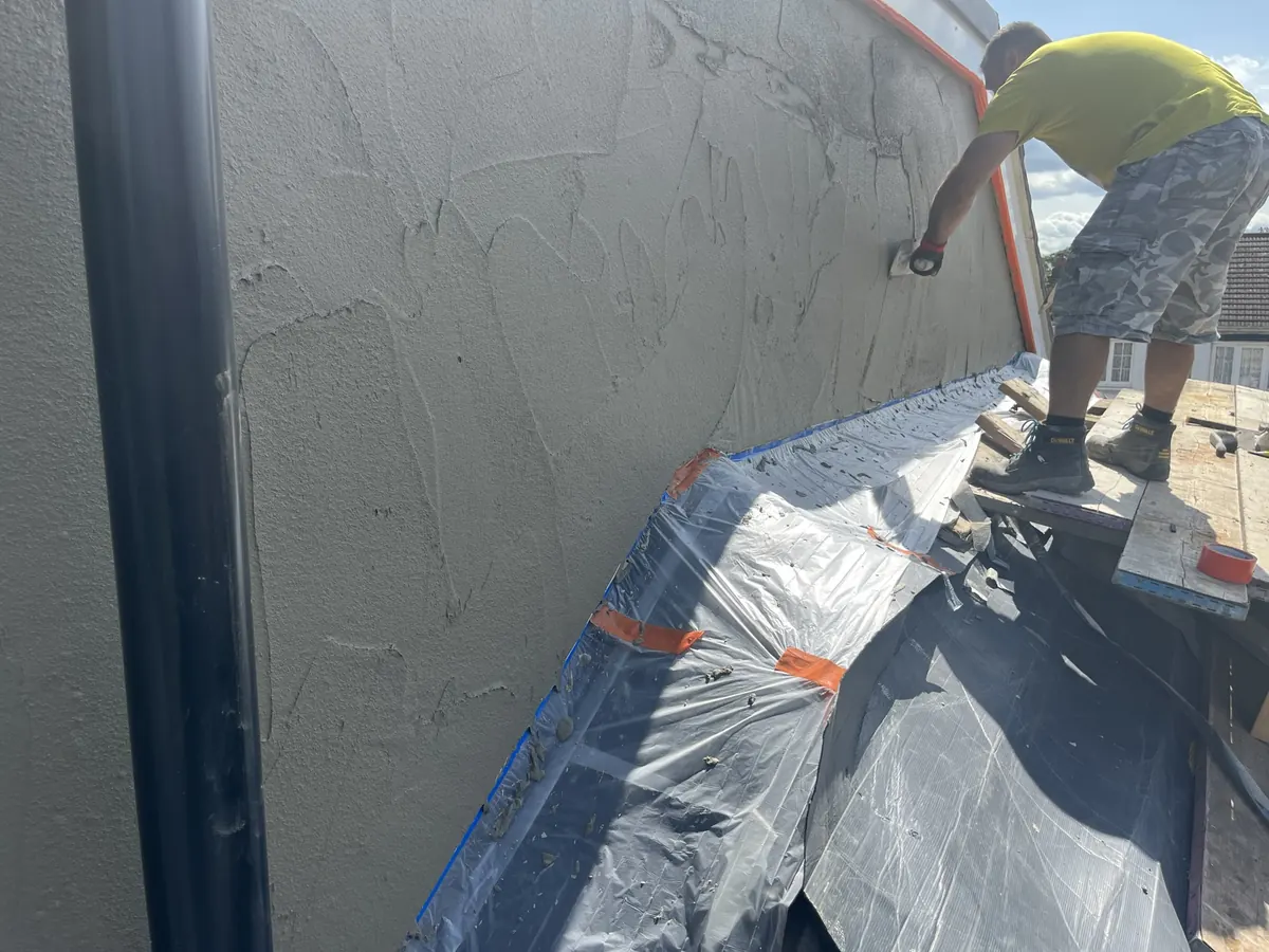 Render being applied by hand to an extension wall in Enfield Town, with the roof protected below
