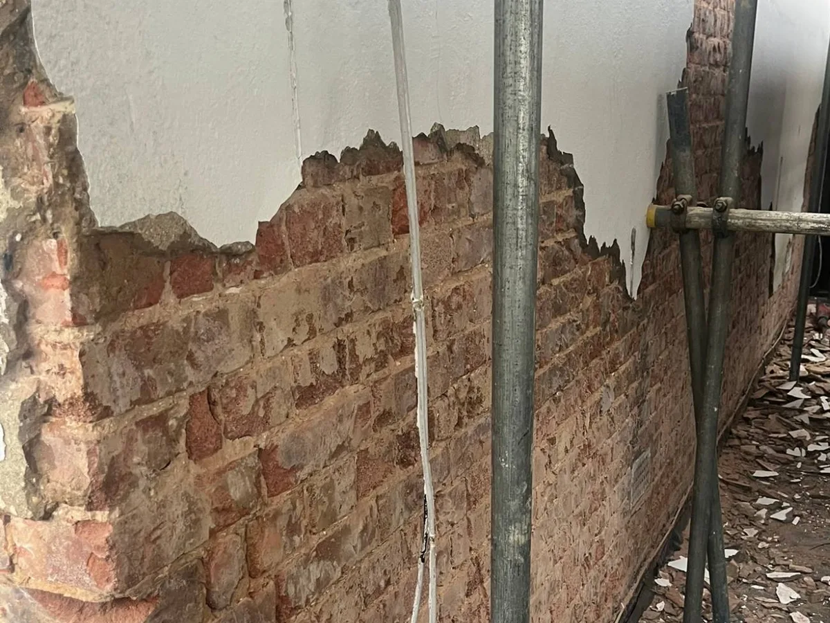 Old painted render being removed from the side wall of a London house, exposing the brickwork underneath