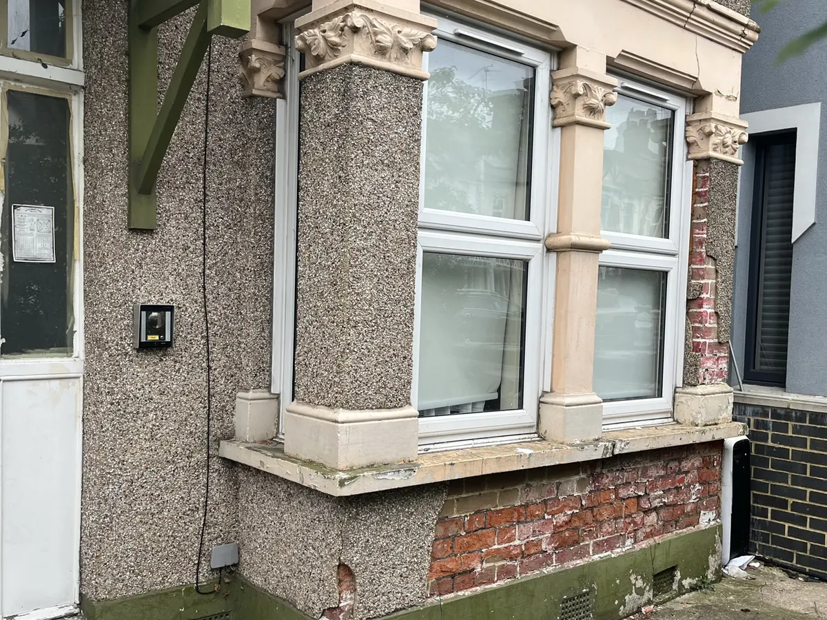 Period bay window with failing pebbledash render and exposed brick below the sill before repair