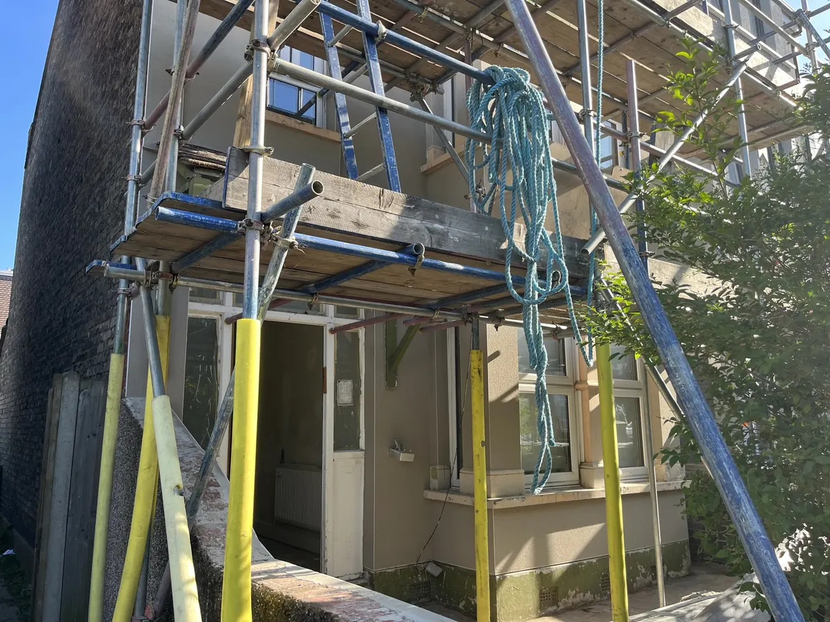 The same house under scaffolding with the old pebbledash removed and new render going on