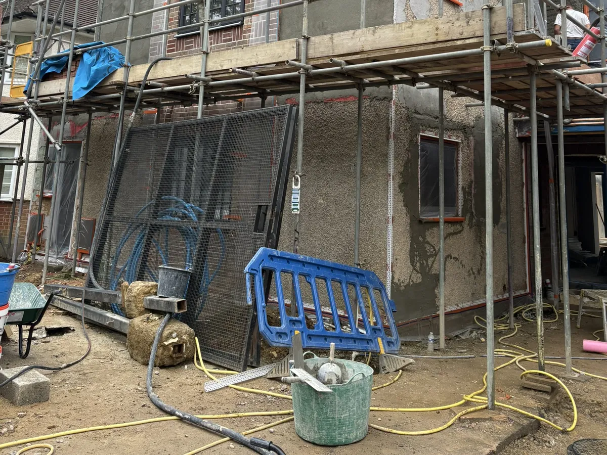 Detached house in St Albans under scaffolding with the first base coat of render applied to the ground floor walls